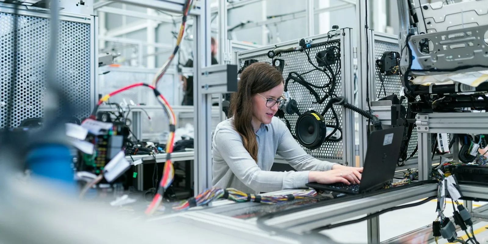 Ingenieurin arbeitet mit Laptop an einer Prüfstation in einer Produktionshalle