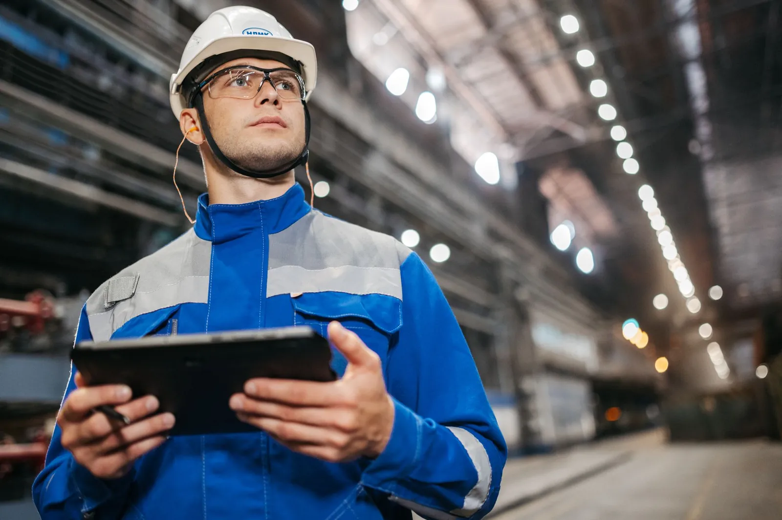 Ingenieur mit Schutzhelm prüft Daten auf einem Tablet in der Werkshalle