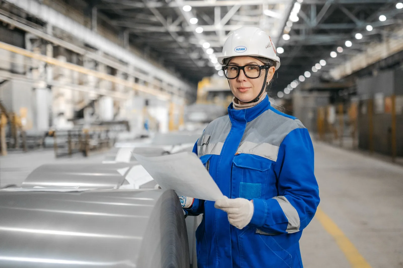 Ingenieurin mit Schutzhelm hält Unterlagen in einer Werkhalle