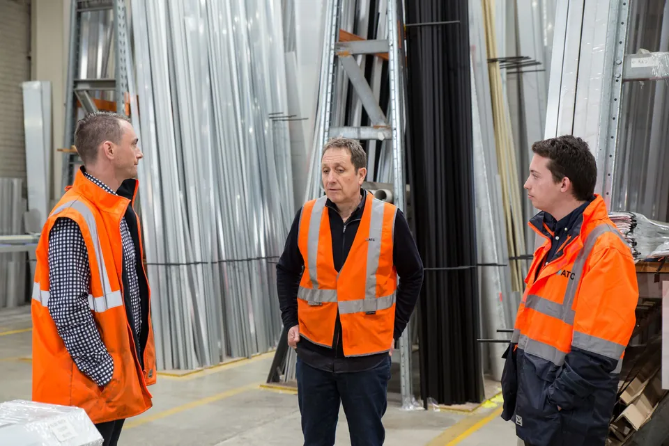 Gespräch zu dritt in einer Werkhalle mit Metallprofilen